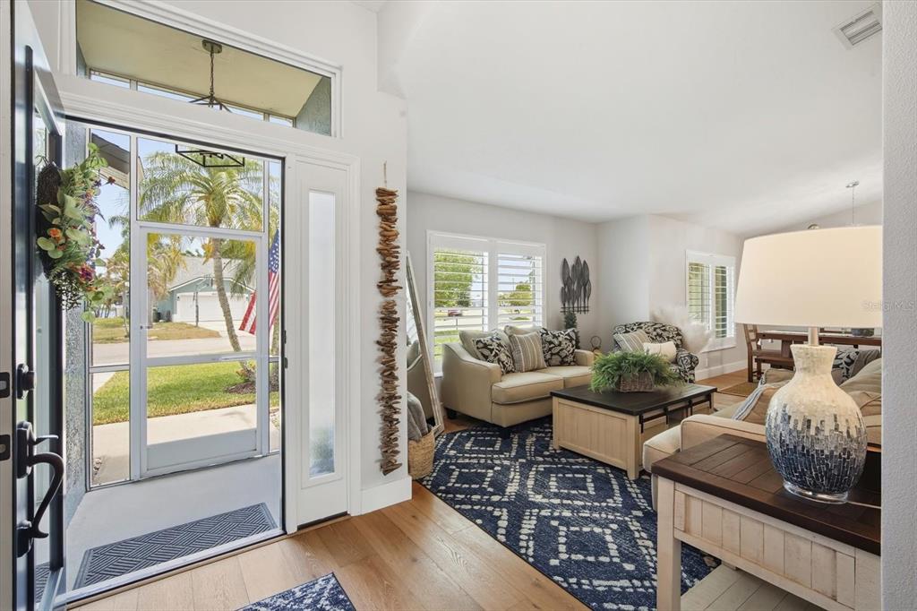 A bright living room features hardwood floors, a blue patterned rug, and an open entryway — 4844 14TH AVENUE E, BRADENTON, FL