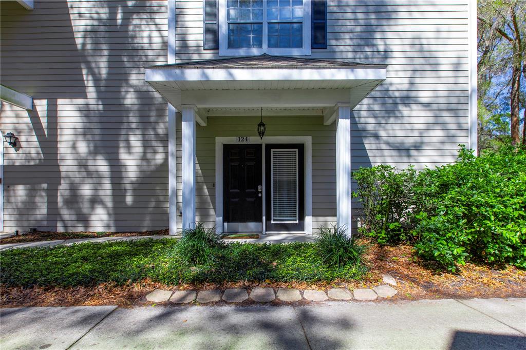 A ground-level view of a residential building entrance with a covered porch and black door — 10000 SW 52ND AVENUE UNIT 124, GAINESVILLE, FL
