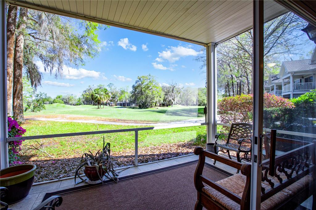 A screened-in porch overlooks a grassy golf course with trees under a blue sky — 10000 SW 52ND AVENUE UNIT 124, GAINESVILLE, FL