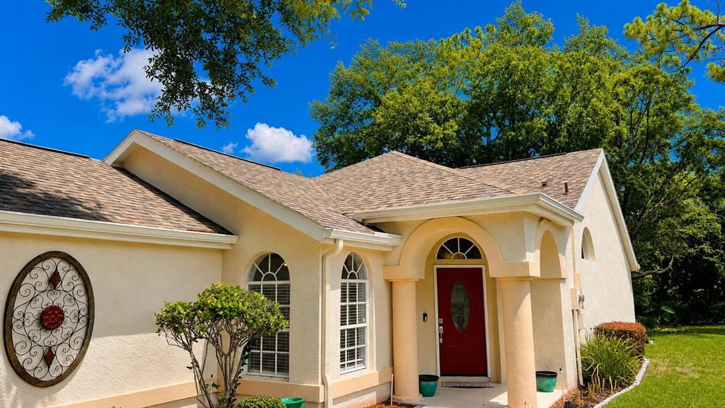 A single-story house with a red front door, arched windows, and a tan stucco exterior — 5556 LEGEND HILLS LANE, SPRING HILL, FL