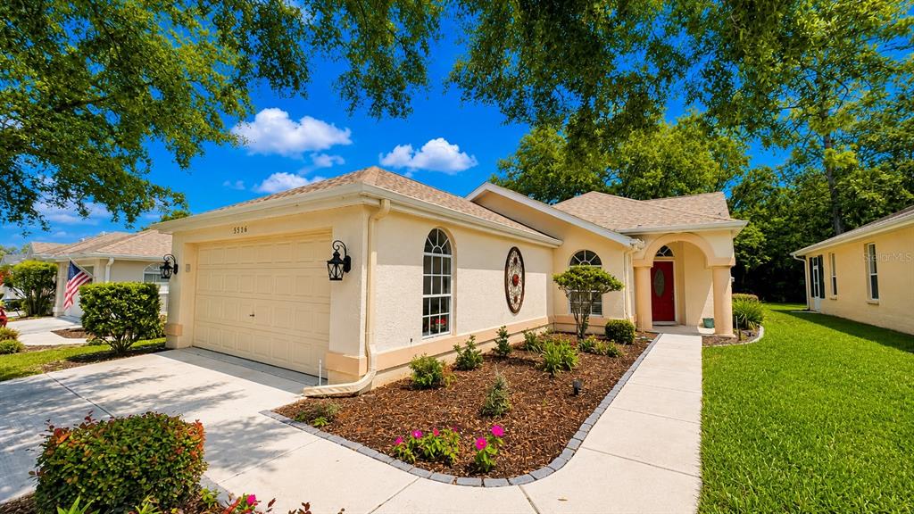 A single-story house with a beige stucco exterior, a two-car garage, and a red door — 5556 LEGEND HILLS LANE, SPRING HILL, FL