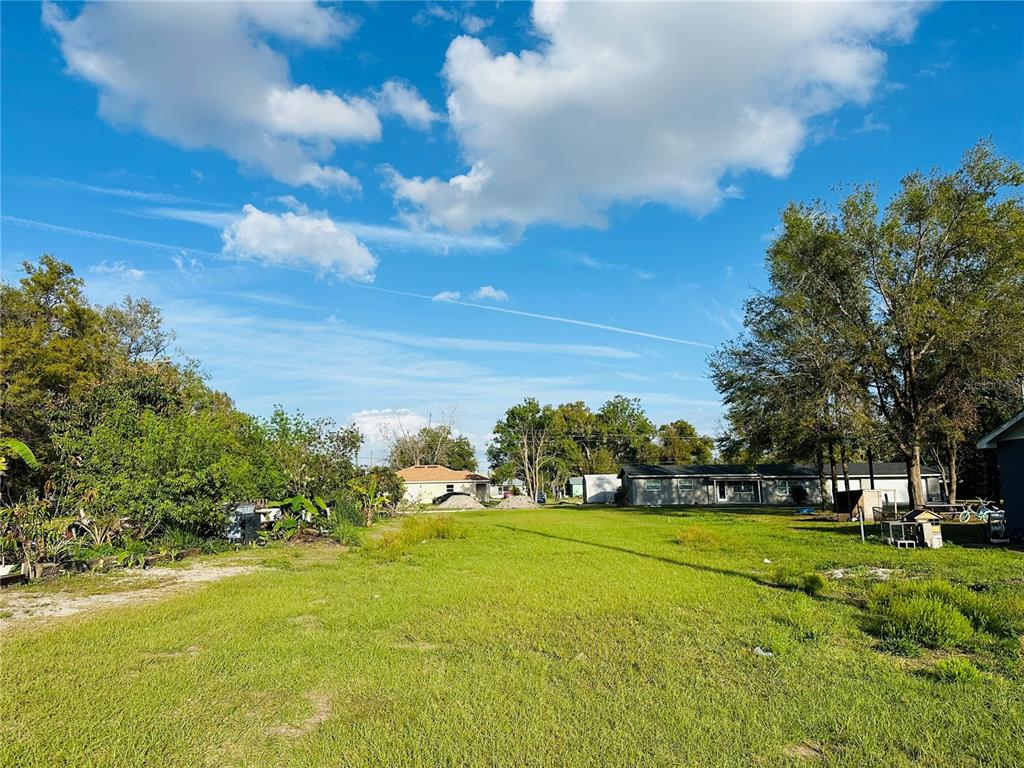A grassy, open residential lot with scattered trees and neighboring houses in the background — 0 RAILROAD AVENUE, FORT MEADE, FL