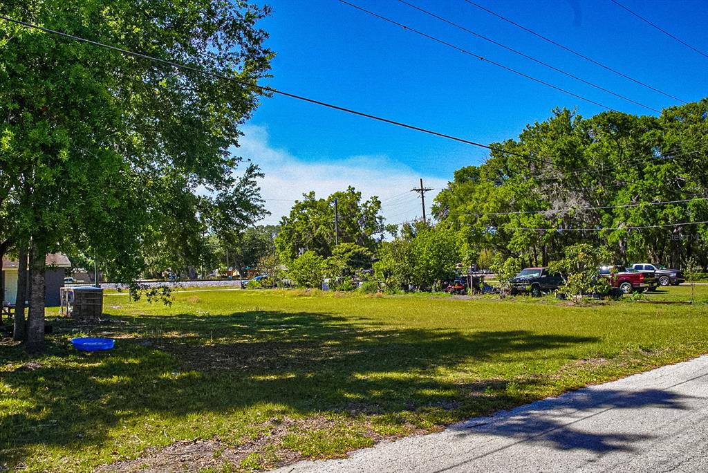 A grassy, open lot features scattered trees, a small shed, and parked vehicles under blue skies — 0 RAILROAD AVENUE, FORT MEADE, FL