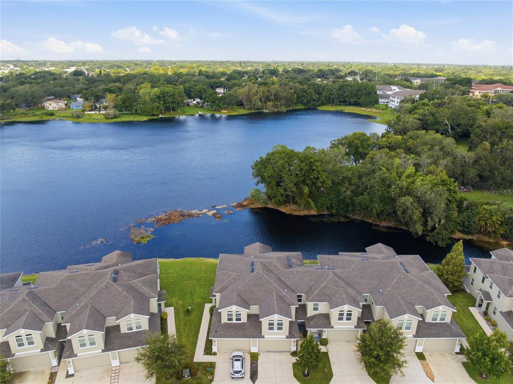 An aerial view shows townhouses with gray roofs situated along the edge of a lake — 1934 LAKE RIDGE BOULEVARD, CLEARWATER, FL