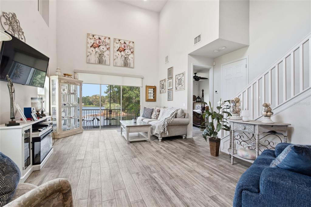 A living room with high ceilings, wood-look tile flooring, and a sliding glass door view — 1934 LAKE RIDGE BOULEVARD, CLEARWATER, FL