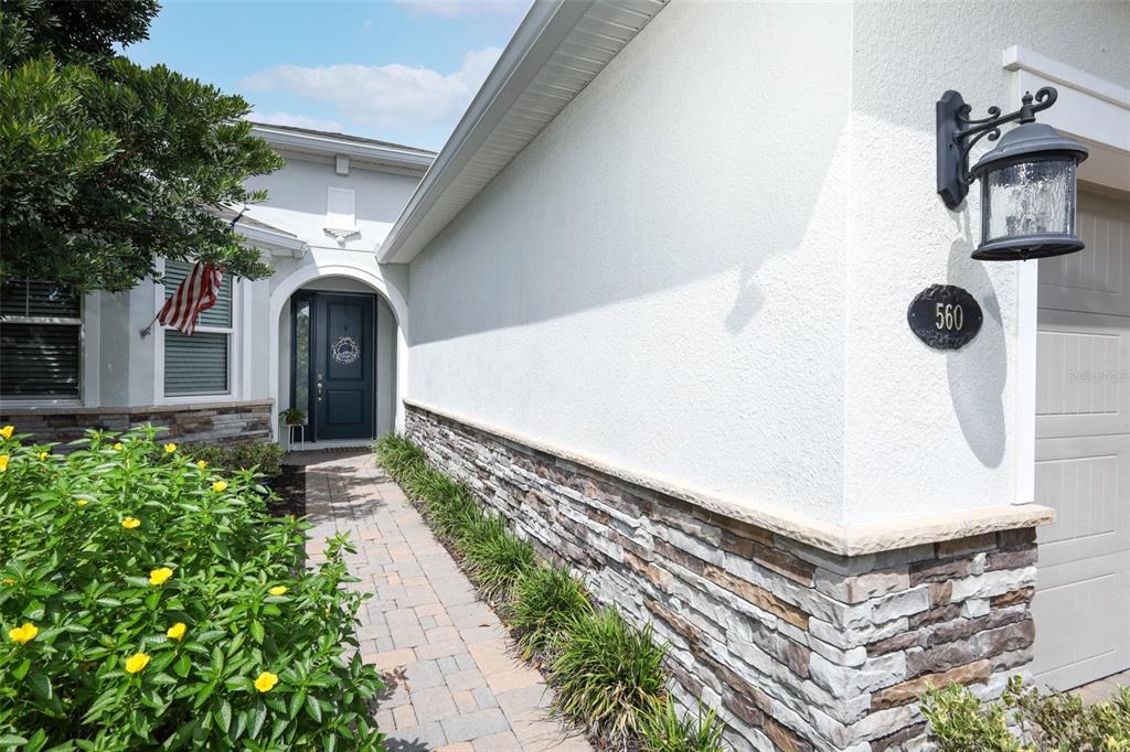 A stone-accented exterior wall leads to a front entryway with a paved walkway — 560 ADENMORE TERRACE, DELAND, FL