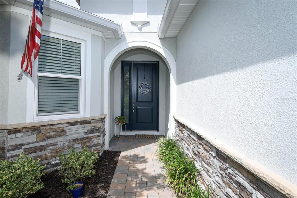 The exterior entryway features a dark blue front door, stone siding, and a paved walkway — 560 ADENMORE TERRACE, DELAND, FL
