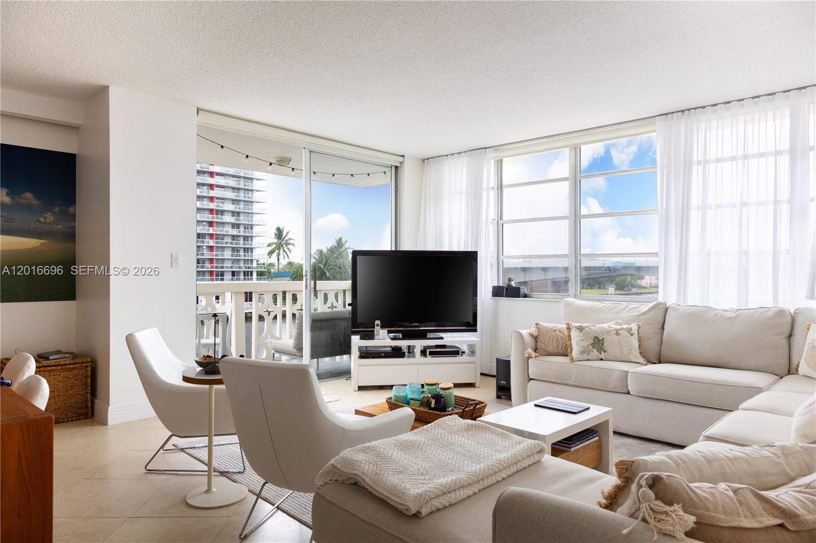 A bright living room features a white sofa, two armchairs, and a balcony with views — 1817 S Ocean Dr # 320, Hallandale Beach FL 33009, HALLANDALE BEACH, FL
