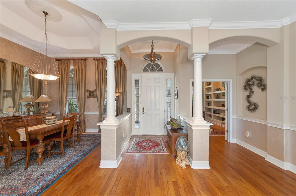 A foyer with hardwood floors, white columns, and an arched entryway leading to a dining room — 10412 WINDING STREAM WAY, BRADENTON, FL