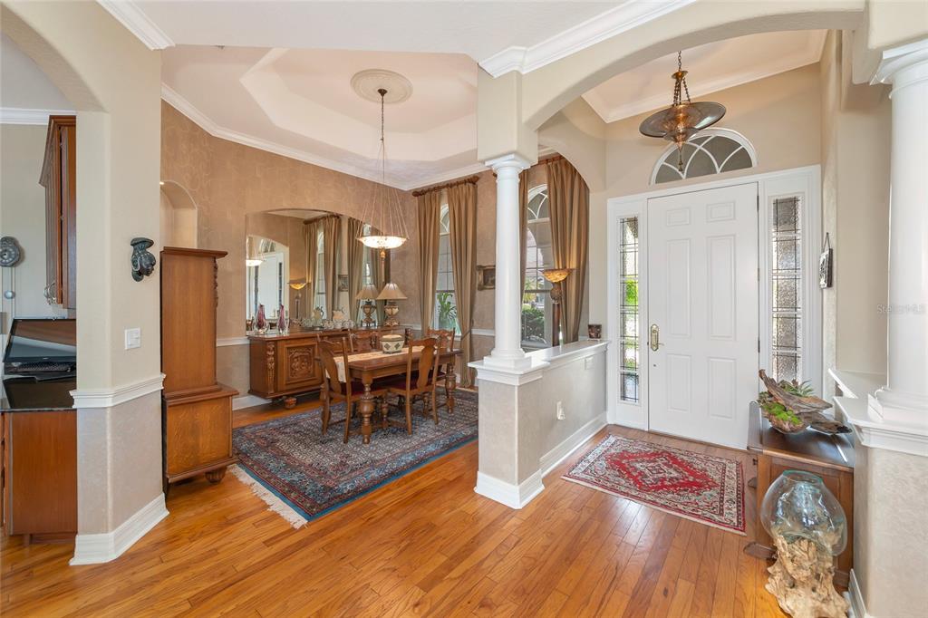 A dining room with a tray ceiling and hardwood floors sits beside a home entryway — 10412 WINDING STREAM WAY, BRADENTON, FL