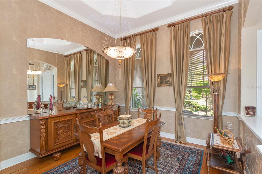 A formal dining room features a wooden table, chairs, a sideboard, and large arched windows — 10412 WINDING STREAM WAY, BRADENTON, FL