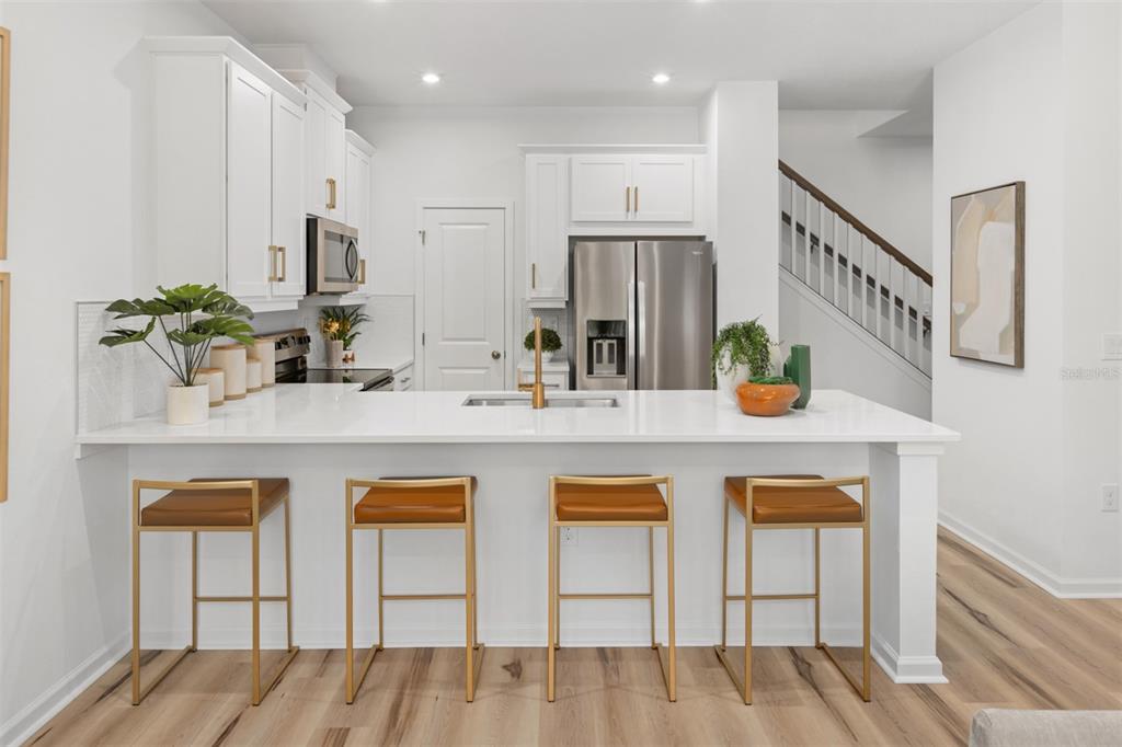 A modern kitchen features white cabinets, stainless steel appliances, a quartz island, and four stools — 1407 TARFLOWER DRIVE, WINTER SPRINGS, FL