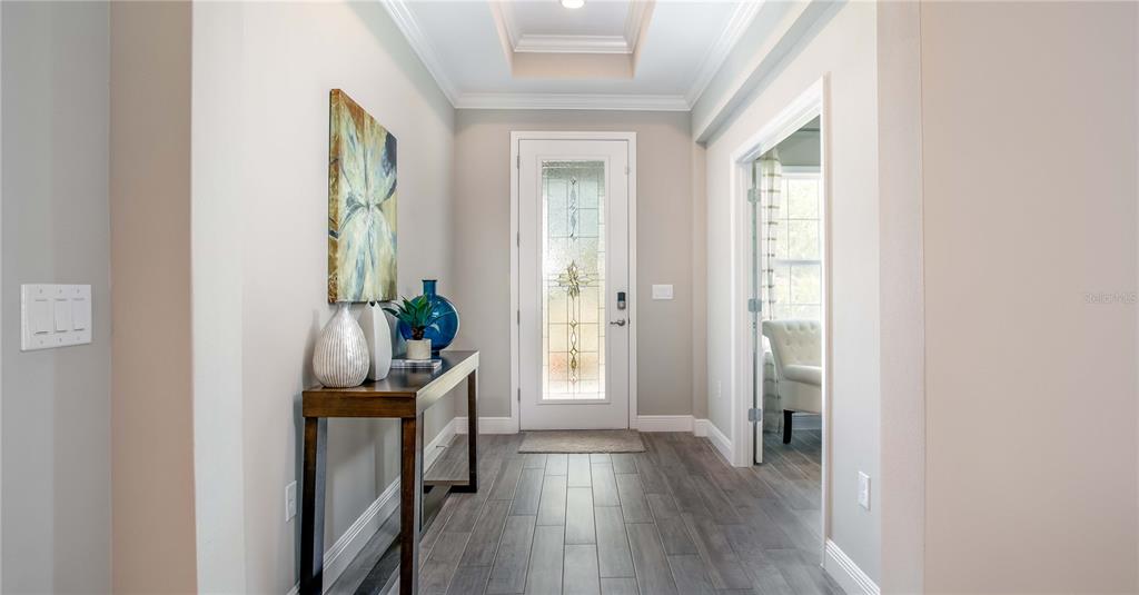 A bright entryway features a wood console table, a glass-paneled front door, and gray flooring — 902 BUCKEYE DRIVE, LADY LAKE, FL