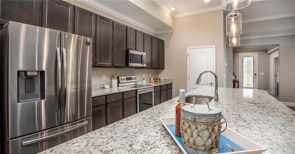 A kitchen features dark wood cabinets, granite countertops, stainless steel appliances, and a central island — 902 BUCKEYE DRIVE, LADY LAKE, FL