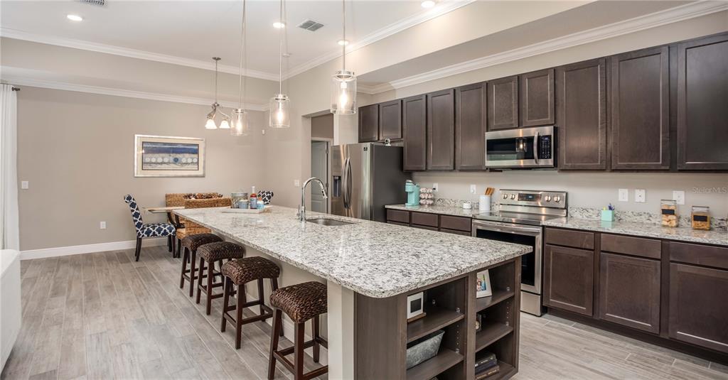A kitchen features dark wood cabinets, granite countertops, a large island, and stainless steel appliances — 902 BUCKEYE DRIVE, LADY LAKE, FL