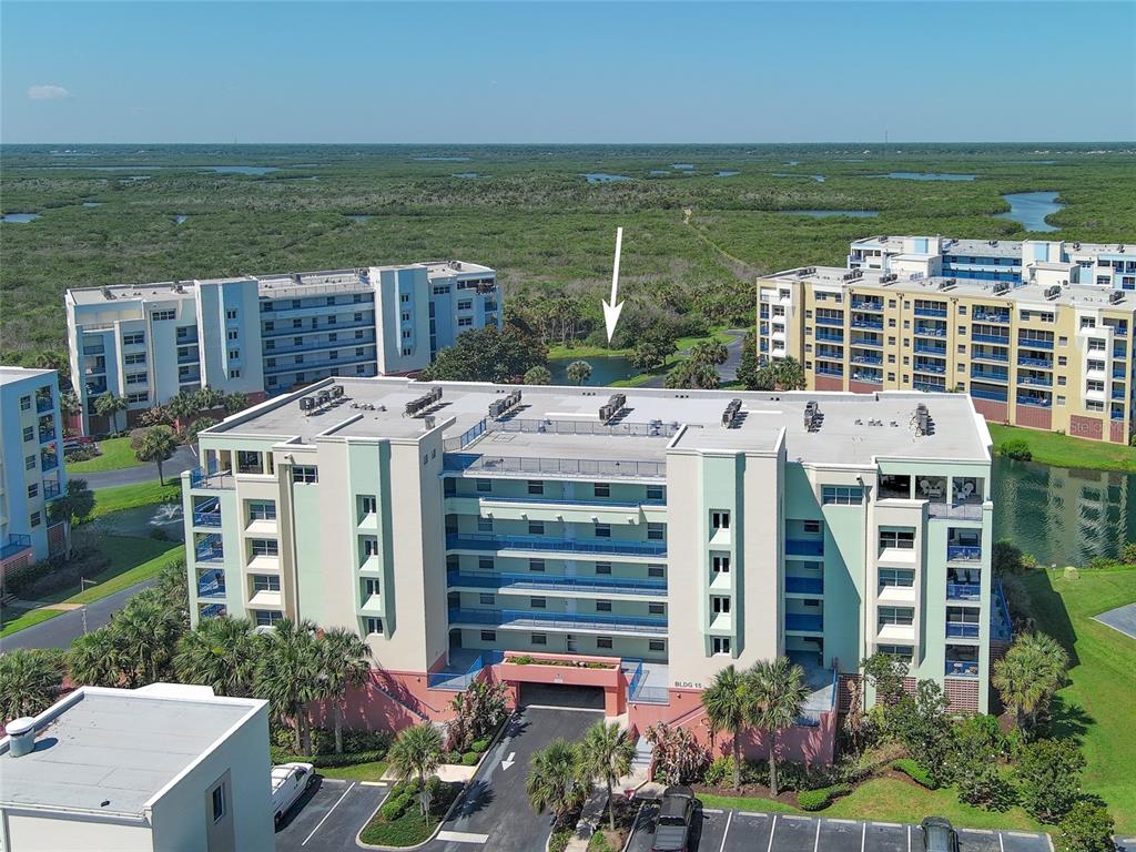 An aerial view shows a multi-story apartment building with a parking lot and surrounding wetlands — 5300 S ATLANTIC AVENUE UNIT 15-203, NEW SMYRNA BEACH, FL