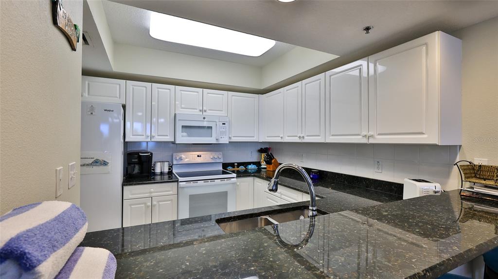 A kitchen features white cabinets, dark granite countertops, a stainless steel sink, and a skylight — 5300 S ATLANTIC AVENUE UNIT 15-203, NEW SMYRNA BEACH, FL