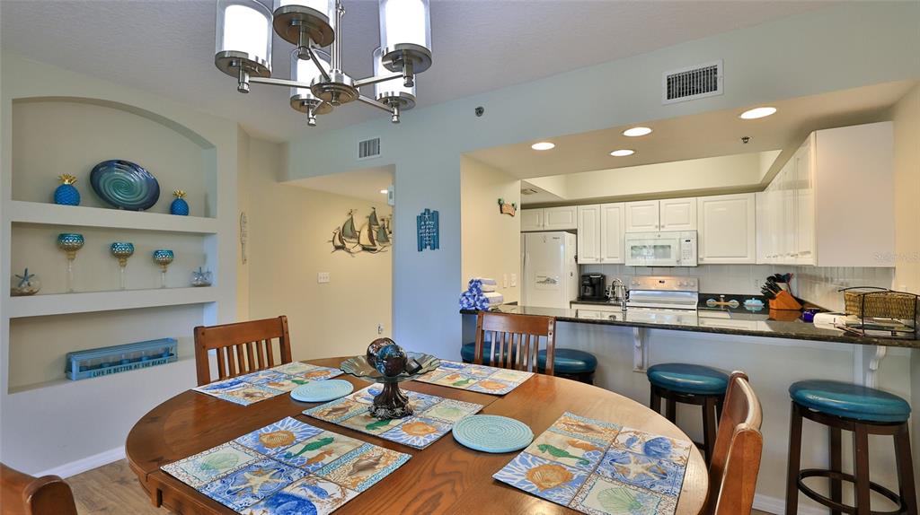 A dining area with a round wooden table sits adjacent to a kitchen with bar seating — 5300 S ATLANTIC AVENUE UNIT 15-203, NEW SMYRNA BEACH, FL