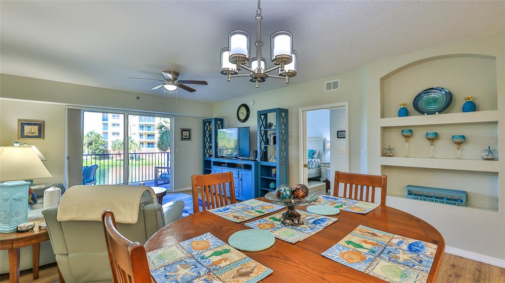 A dining area with a wooden table and chairs sits before a living room with a balcony — 5300 S ATLANTIC AVENUE UNIT 15-203, NEW SMYRNA BEACH, FL