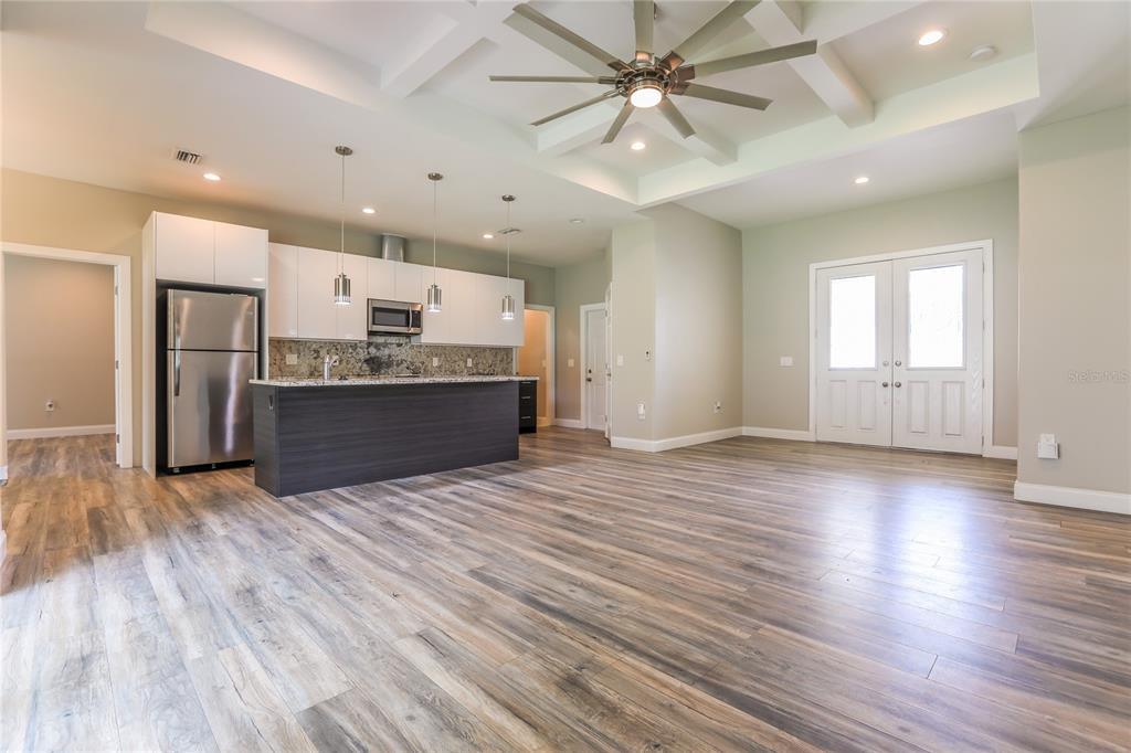 A modern kitchen with white cabinets and a dark island opens into a spacious living area — 2369 MISTLETO LANE, NORTH PORT, FL