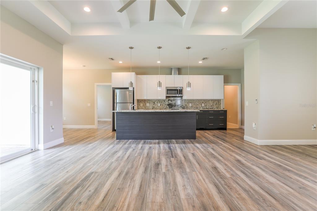 A modern kitchen features white upper cabinets, dark lower cabinets, a granite island, and wood-look flooring — 2369 MISTLETO LANE, NORTH PORT, FL