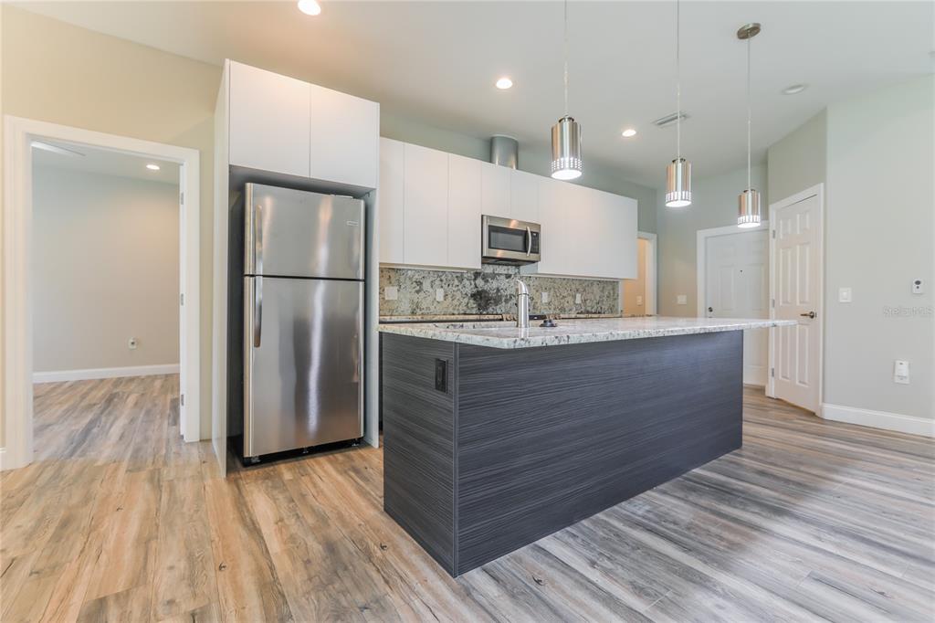 A modern kitchen features a dark wood island, white cabinetry, stainless steel appliances, and wood-look flooring — 2369 MISTLETO LANE, NORTH PORT, FL