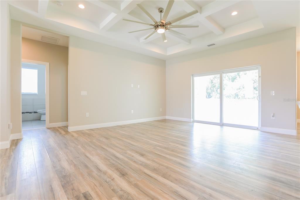 A bright living room features light wood-look flooring, a coffered ceiling, and sliding glass doors — 2369 MISTLETO LANE, NORTH PORT, FL