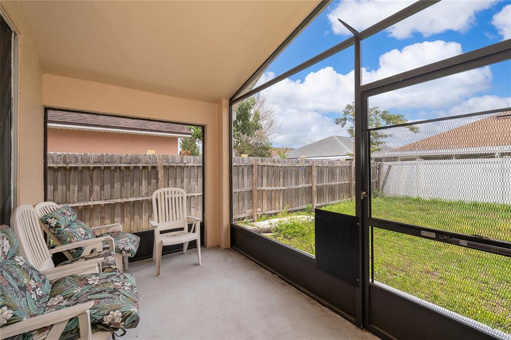 A screened-in patio with concrete flooring, white plastic chairs, and a view of the backyard — 7978 ELMSTONE CIRCLE, ORLANDO, FL
