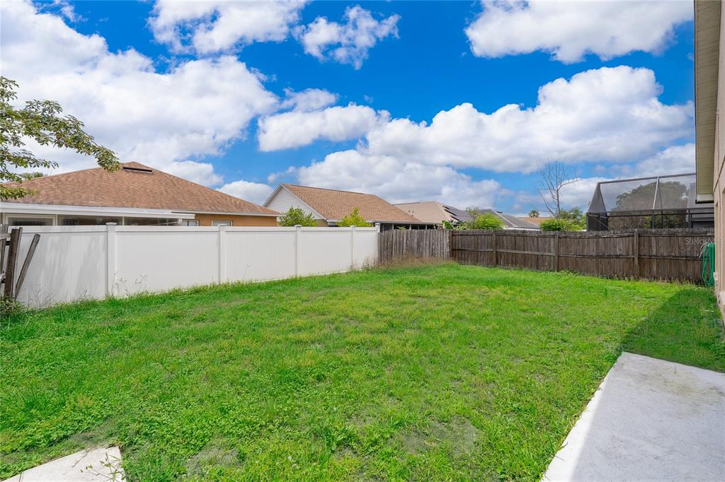 A grassy backyard features a white vinyl fence, a wooden fence, and a concrete patio — 7978 ELMSTONE CIRCLE, ORLANDO, FL