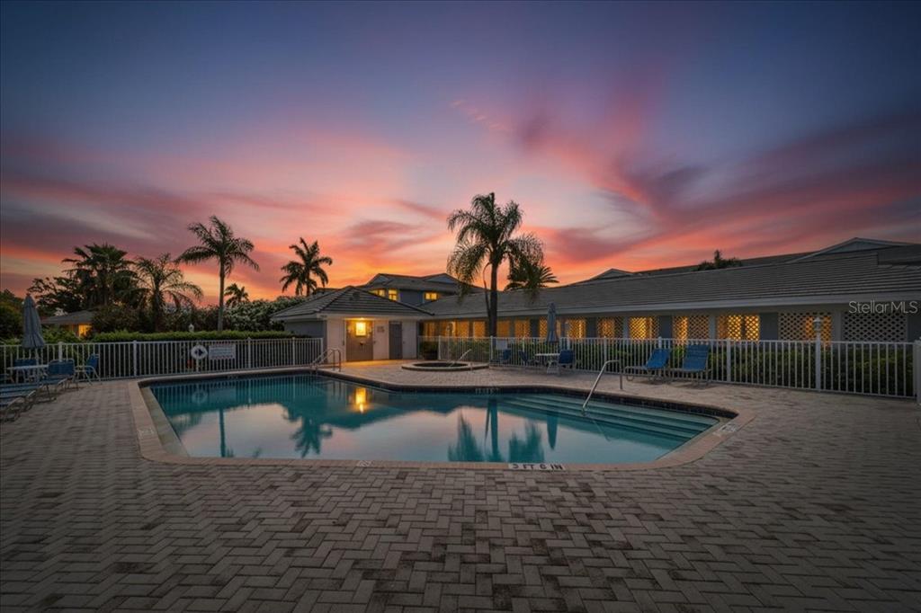 A swimming pool with a paved deck sits in front of a building at sunset — 1343 PERICO POINT CIRCLE UNIT 117, BRADENTON, FL