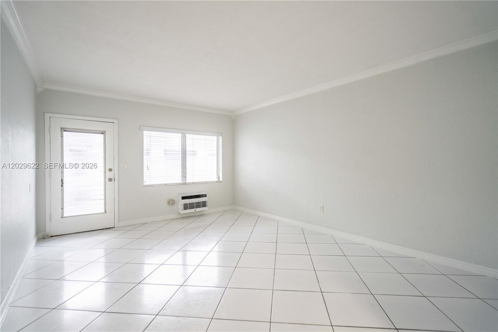 A bright, empty room features white tiled floors, a window, and a glass-paneled door — 7640 Carlyle Ave # 9B, Miami Beach FL 33141, MIAMI BEACH, FL