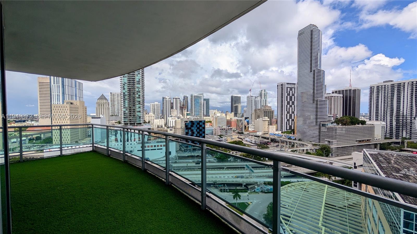 A balcony with artificial turf flooring overlooks a dense city skyline and highway interchange — 350 S Miami Ave # 1901, Miami FL 33130, MIAMI, FL