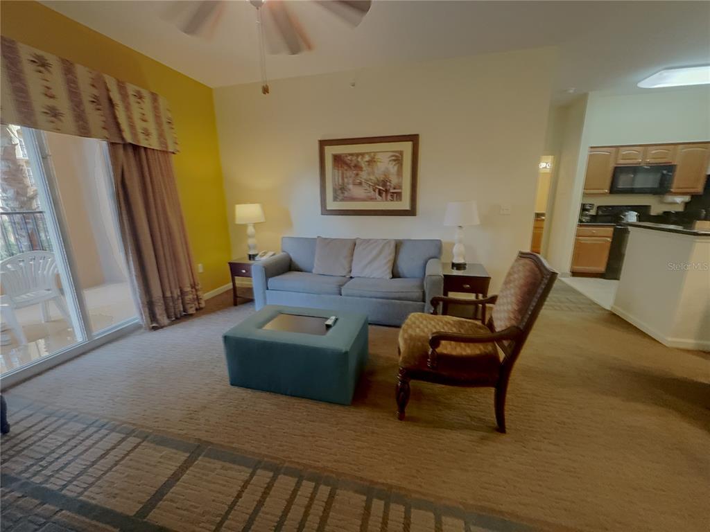 A living room features a blue sofa, a matching ottoman, and an adjacent kitchen area — 8125 RESORT VILLAGE DRIVE UNIT 5304, ORLANDO, FL