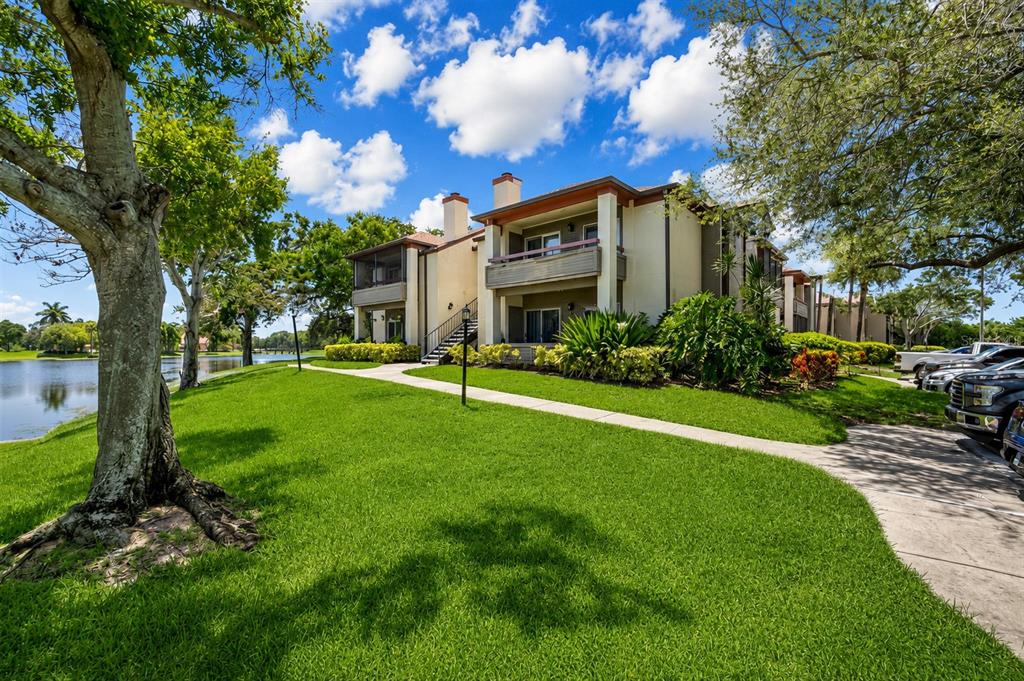 A multi-story apartment building sits beside a lake with a lawn and parking area — 10263 GANDY BOULEVARD N UNIT 2116, ST PETERSBURG, FL