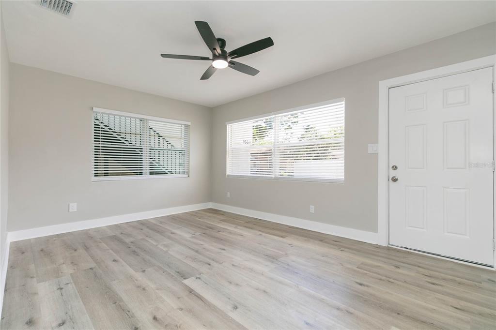 An empty room features light gray walls, wood-look flooring, a ceiling fan, and a white door — 2600 52ND AVENUE N UNIT B, ST PETERSBURG, FL