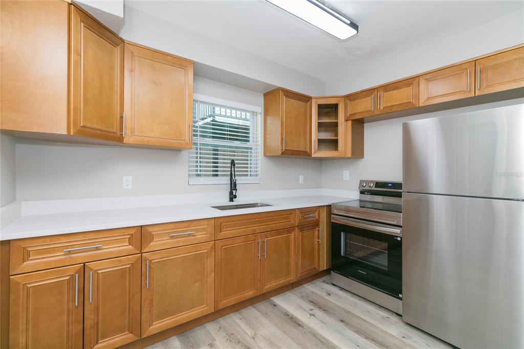 A kitchen features light wood cabinets, stainless steel appliances, white countertops, and wood-look flooring — 2600 52ND AVENUE N UNIT B, ST PETERSBURG, FL