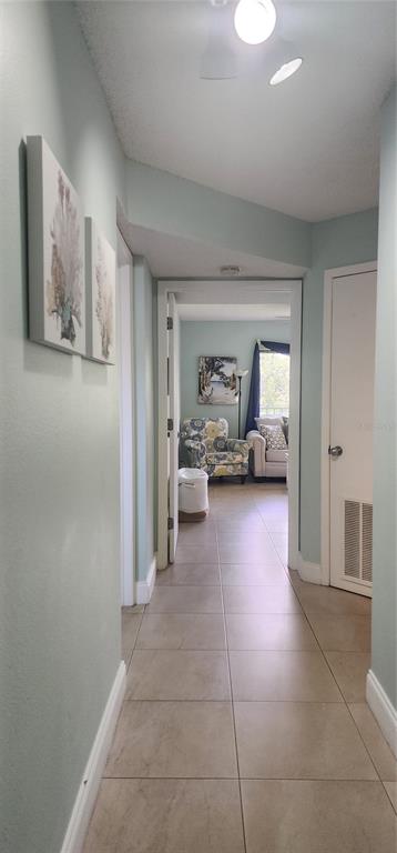 A hallway with light blue walls and tile flooring leads to a living area beyond — 1515 PINELLAS BAYWAY S UNIT 62, TIERRA VERDE, FL