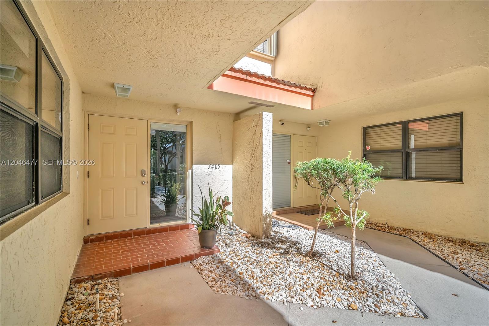 An exterior entryway features a brick porch, a small tree, and gravel landscaping — 3405 Emerald Oaks Dr # 207, Hollywood FL 33021, HOLLYWOOD, FL
