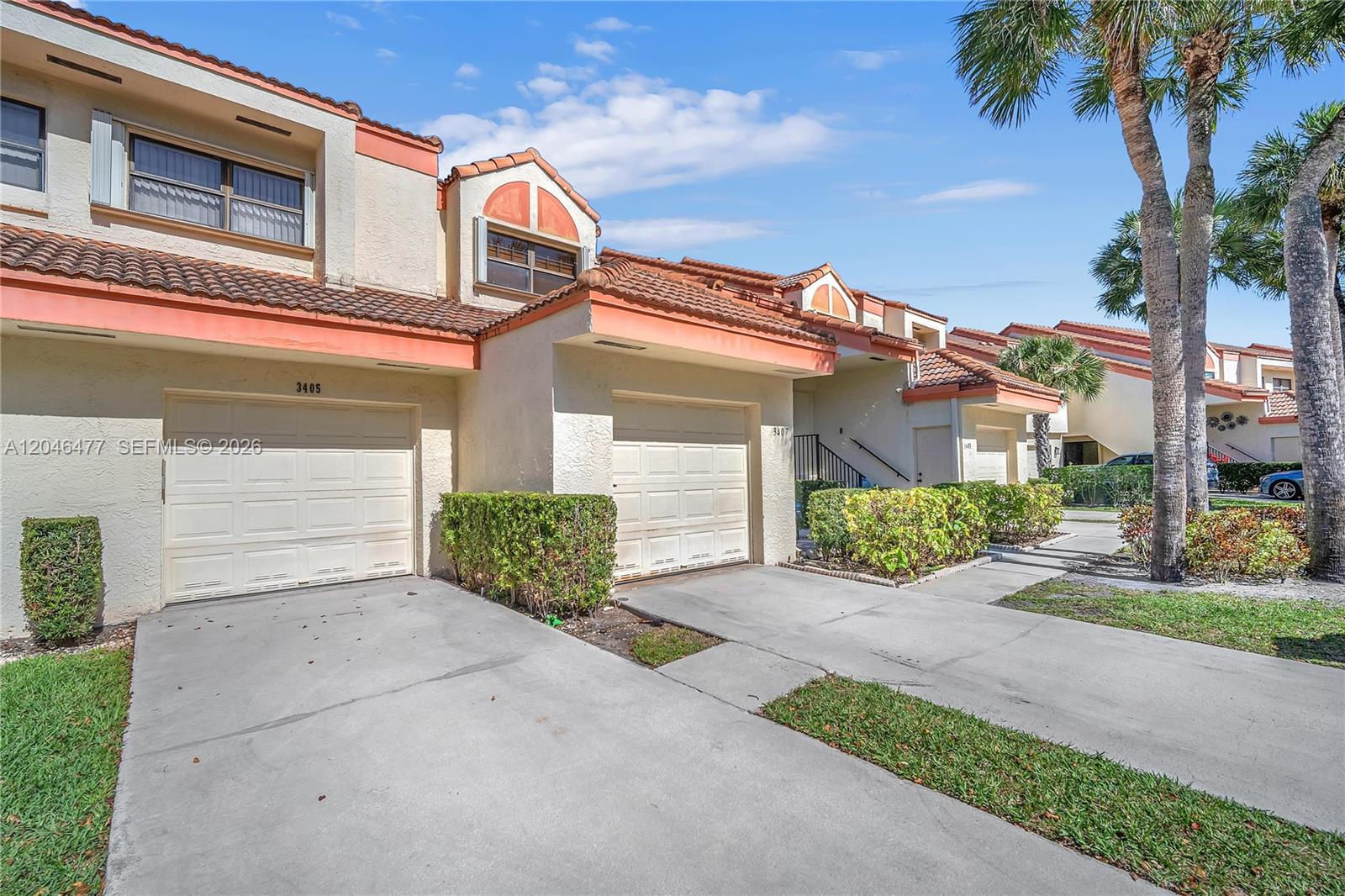 A row of attached townhomes features beige stucco walls, tile roofs, and private garage doors — 3405 Emerald Oaks Dr # 207, Hollywood FL 33021, HOLLYWOOD, FL