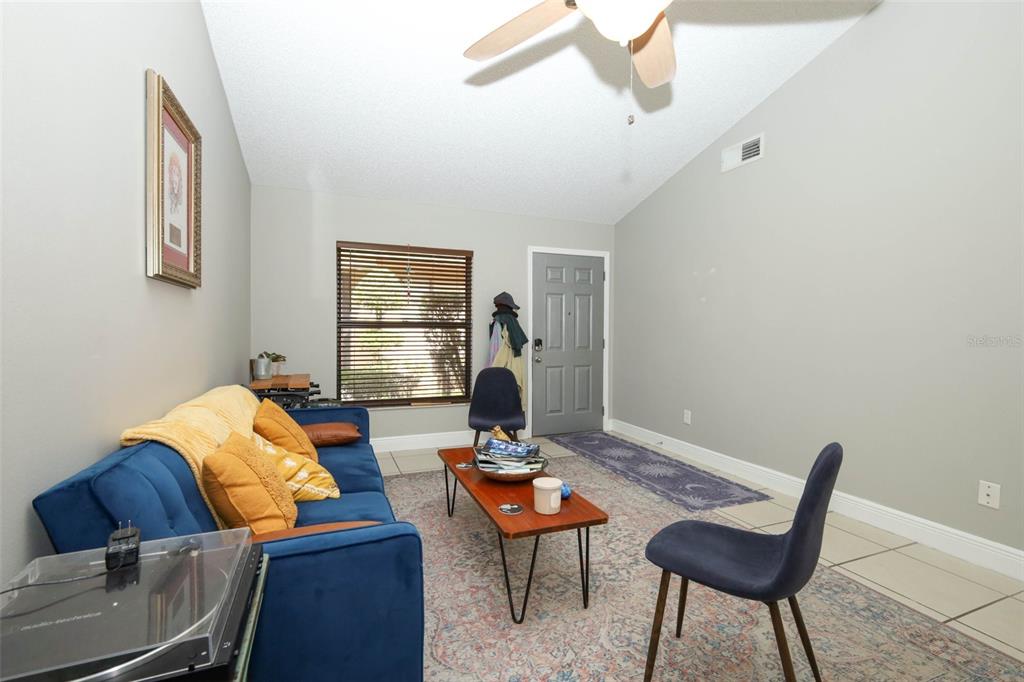 A living room features a blue sofa, a coffee table, two chairs, and tile flooring — 359 DOUGLAS WAY UNIT 54, WINTER GARDEN, FL