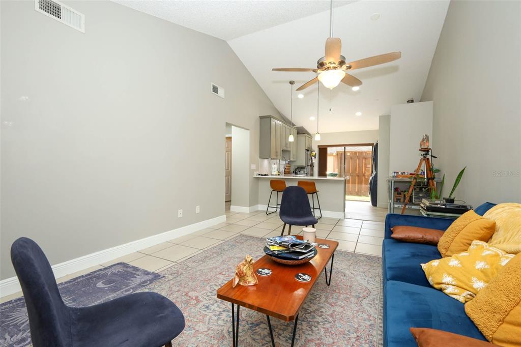 A living room with a vaulted ceiling, tile flooring, and an open kitchen with bar seating — 359 DOUGLAS WAY UNIT 54, WINTER GARDEN, FL
