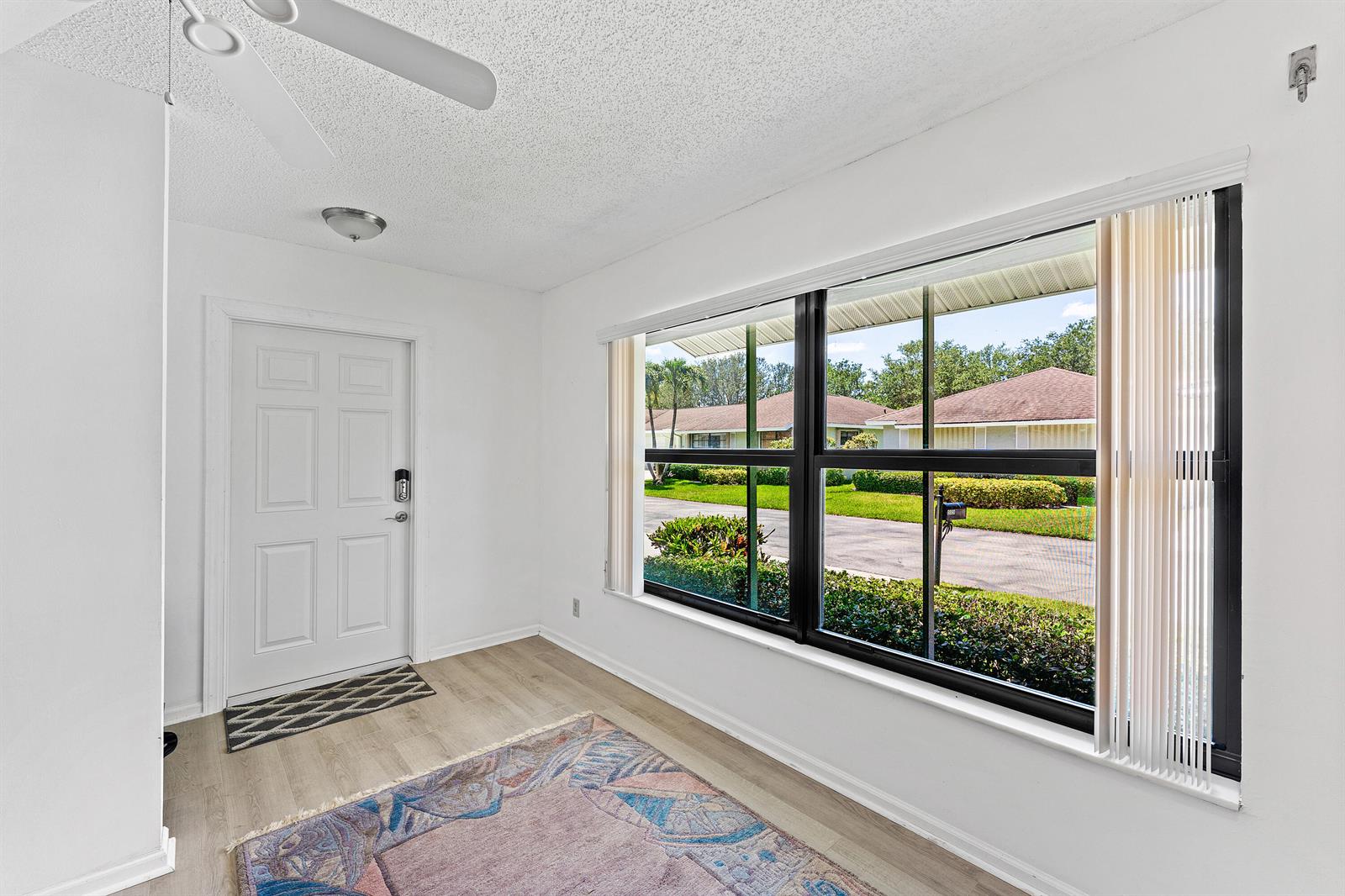 A bright room with white walls, light wood-look flooring, a ceiling fan, and large windows — 9890 Papaya Tree Trail # A, Boynton Beach FL 33436, BOYNTON BEACH, FL