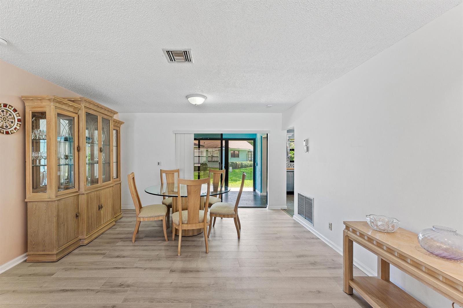 A dining room with a glass table, wooden hutch, and sliding doors to a backyard — 9890 Papaya Tree Trail # A, Boynton Beach FL 33436, BOYNTON BEACH, FL