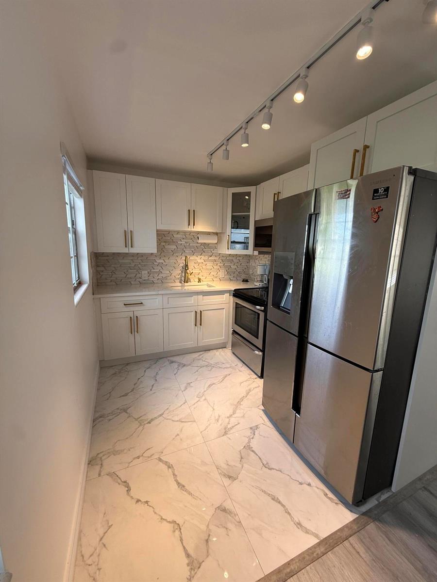A galley kitchen features white cabinets, marble-patterned tile flooring, and stainless steel appliances — 389 Fanshaw J # 389, Boca Raton FL 33434, BOCA RATON, FL