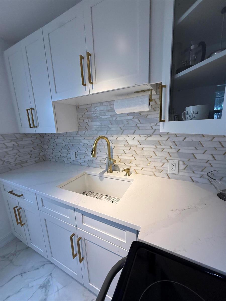 A kitchen features white cabinets, gold hardware, a marble backsplash, and a white farmhouse sink — 389 Fanshaw J # 389, Boca Raton FL 33434, BOCA RATON, FL