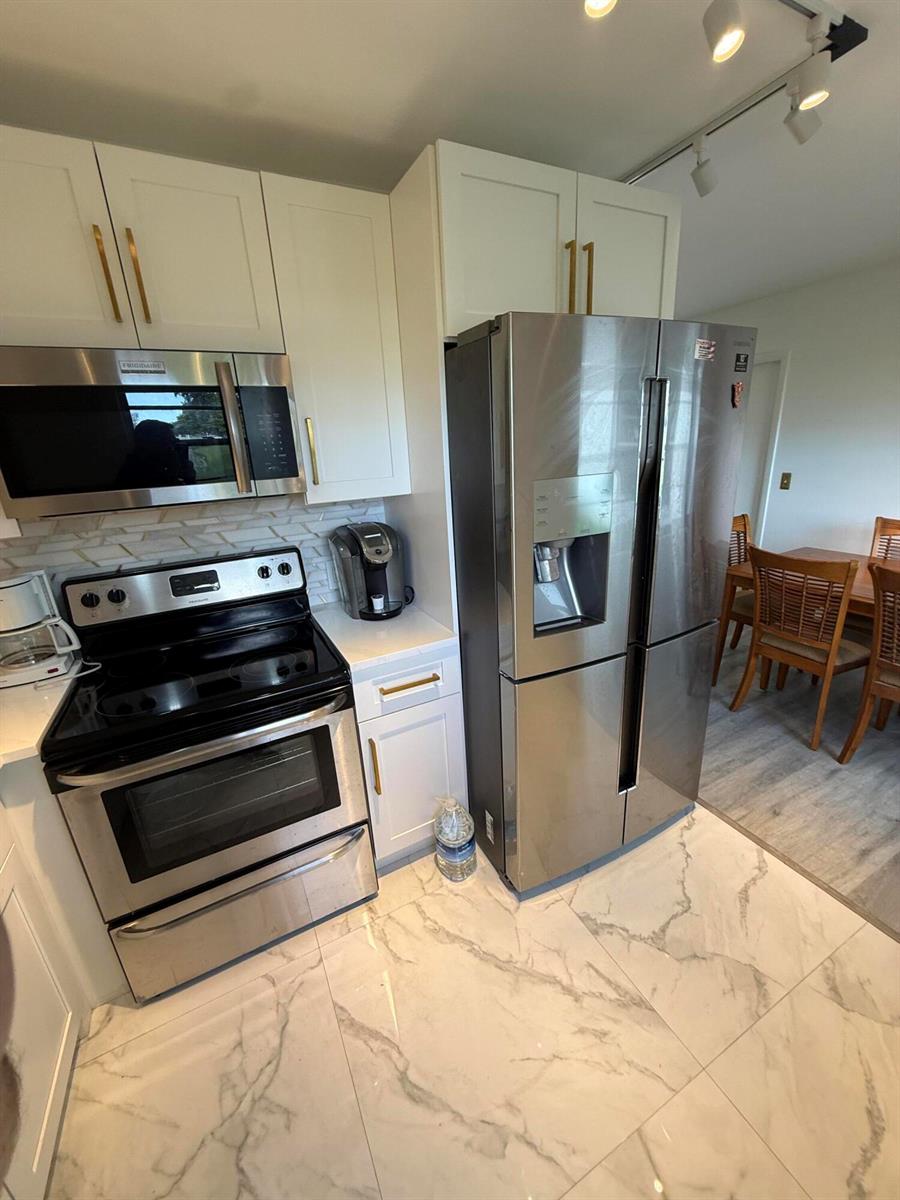 A kitchen features white cabinets, stainless steel appliances, and white marble-patterned tile flooring — 389 Fanshaw J # 389, Boca Raton FL 33434, BOCA RATON, FL