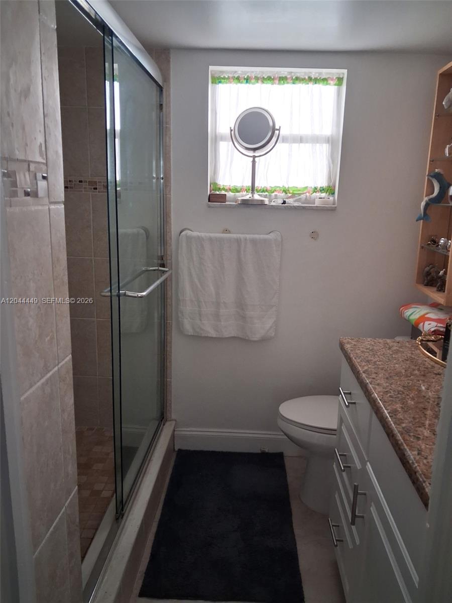 A bathroom features a glass-enclosed shower, a white vanity with a granite countertop, and a toilet — 410 SE 2nd St # 307, Hallandale Beach FL 33009, HALLANDALE BEACH, FL