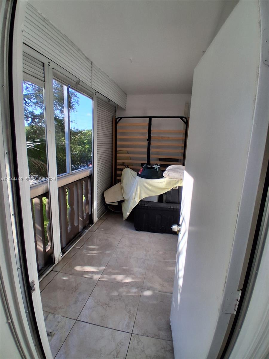 A tiled balcony features sliding glass doors, a wooden railing, and stored furniture — 410 SE 2nd St # 307, Hallandale Beach FL 33009, HALLANDALE BEACH, FL
