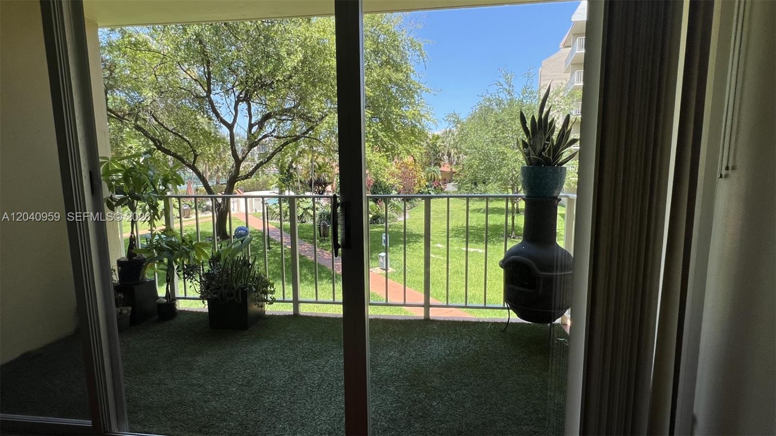A balcony with artificial turf overlooks a grassy courtyard with trees and a walkway — 13120 SW 92nd Ave # 209, Miami FL 33176, MIAMI, FL