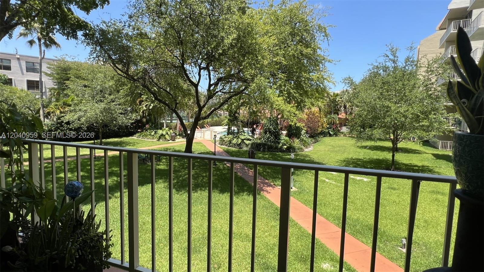 A balcony view overlooks a grassy courtyard with a paved walkway and mature trees — 13120 SW 92nd Ave # 209, Miami FL 33176, MIAMI, FL